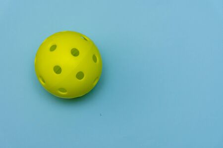 Bright yellow pickleball or whiffle ball on a solid aqua blue flat lay background symbolizing sports and activity with copy space.の写真素材