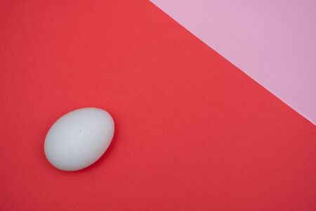 Easter holiday flat lay with white egg on a solid bright red and pink vibrant background with copy space.の写真素材
