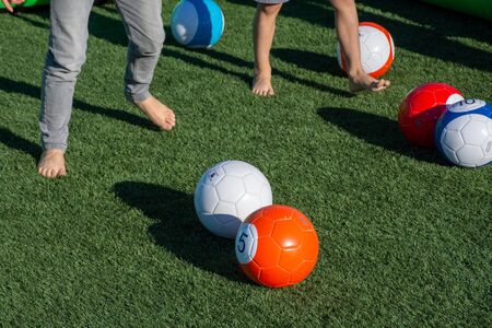 Vibrant billiards soccer/footballs balls on the green grass with children's feet kicking for...