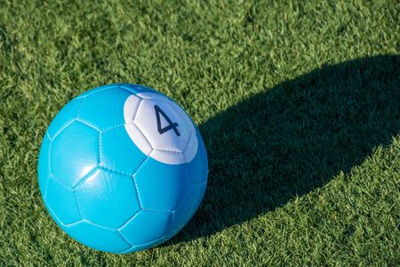 Blue number 4 soccer billiards or pool ball on green grass with a shadow and copy space. Concept of...