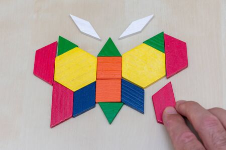 Tangram butterfly colored child geometric puzzle piece with hand filling in final piece on brown...