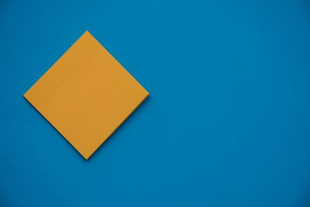 Bright orange posted note on bright blue flat lay background for education or business organization and reminder concepts.の写真素材