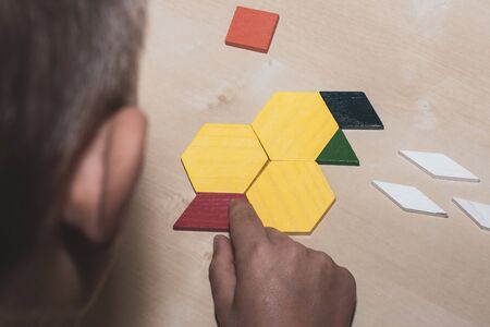 Tangram geometric colored shapes puzzle piece looking over child's shoulder to pieces on brown table. Education and problem solving concept.の写真素材