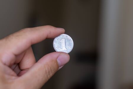 Persons hand holding out a one reminbi (RMB) or Yuan, the Currency of China -  on a brown...