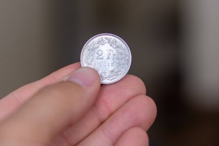 Persons hand holding out a silver two franc coin, the Currency of the Switzerland -  on a brown background. Money exchange.の写真素材