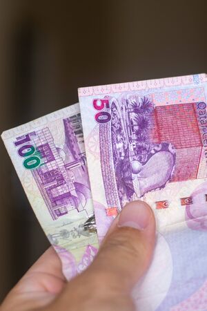 Persons hand giving the Currency of the Qatar - One fifty and hundred rial or riyal note spread out...
