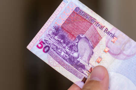 Persons hand giving the Currency of the Qatar - One fifty rial or riyal note spread out on a brown background. Money exchange.の写真素材
