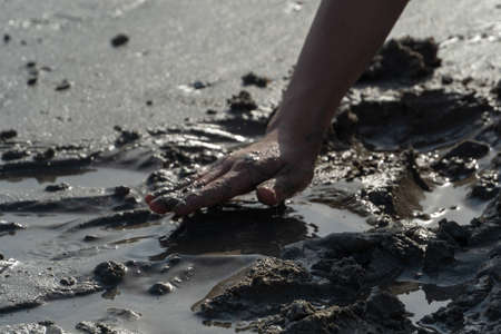 Sihouette of a child's hand playing in the mud or sand at the beack on a sunny day.の写真素材