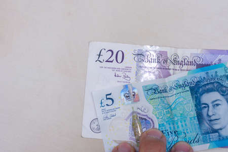 Persons hand giving the Currency of the England in the United Kingdom - One purple twenty pound and blue five pound note spread out on a white background. Money exchange.の写真素材