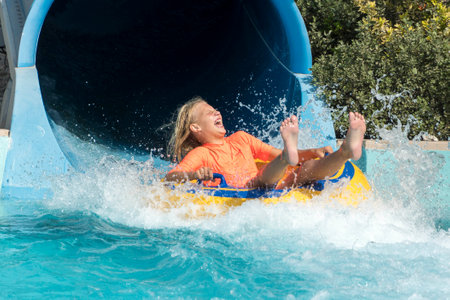 Girl on water slide inner tube splashing in the water with joy and laughter for summer travel fun.の写真素材