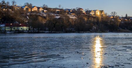 Southern Bug River in winter. The ice began to melt on the river. The setting sun is reflected in...