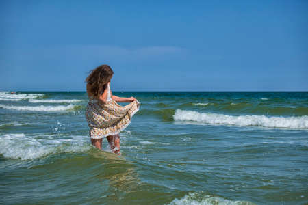 Young girl stands in the sea, lifting the edge of a sundress so that it would not be wetの写真素材