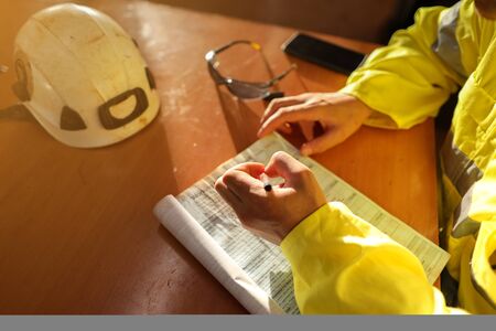 Top view of young construction gold miner worker hand holding pen writing job hazards analysis on...