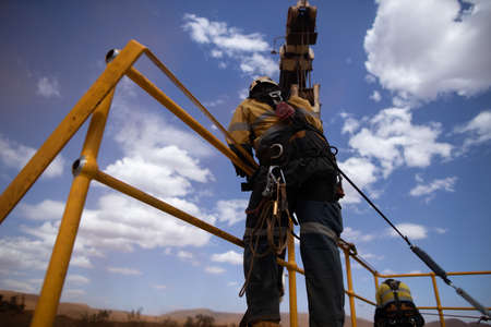Safe workplace rigger wearing working at heights harness clipping an inertia reel shock absorbing...