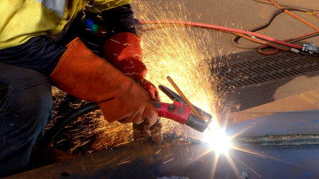 Construction miner setting wearing a safety helmet, red welding leather glove dark face shield protection while commencing hot work gouging metal plate on the ground surface constrの写真素材