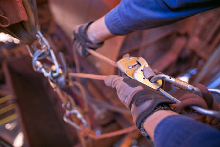 Male rope access technician inspector hand wearing a safety glove performing inspecting descender ensure rope is lock connecting correctly on rope prior to abseiling constructionの写真素材