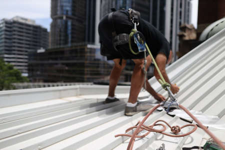 Construction worker wearing safety harness using secondary safety device connecting into 10.5 mm static rope using as fall restraint repairing roof leak working positioning on topの写真素材