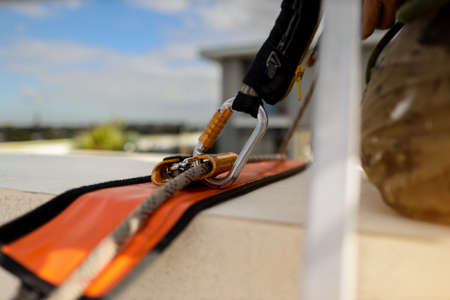 Construction industrial rope access abseiler window cleaner worker bend knees while going over the ledge using fall arrester safety energy shock absorbing lanyard backup deviceの写真素材