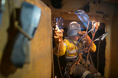 Rope access welder wearing fully safety uniform fall protection helmet, welding glove harness,...
