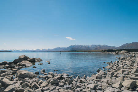 Lakeside with rock and blue sky and mountainの写真素材
