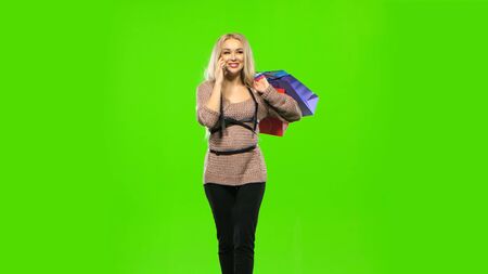 Blonde girl carries a multi colored packages, talking on the phone and smiles sweetly. Green screenの写真素材