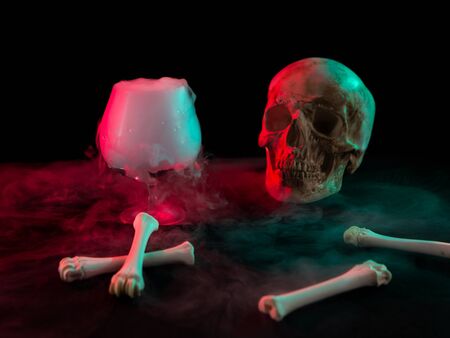 Human skull near glass with thick smoke and bones for Day of the Dead on dark background with red light.の写真素材