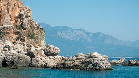 Beautiful deep sea with small waves, steep cliffs on shores of Mediterranean Sea with trees and caves against mountains in distance. Sea cruise on ship or yacht along rocky shore with beautiful natureの写真素材