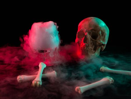 Human skull near glass with thick smoke and bones for Day of the Dead on dark background with red light.の写真素材
