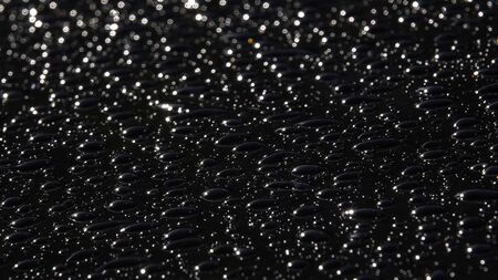 Drops of rain on a black background. Droplets of water on black glass background running. Blurred...