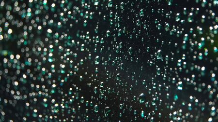 Drops of rain on a black background. Droplets of water on black glass background running. Blurred...