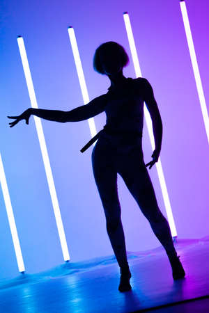 Young stylish girl dancing in the Studio on a colored background with neon lighting lamp. Music dj poster design. Dark silhouette.の写真素材
