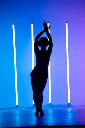 Young stylish girl dancing in the Studio on a colored background with neon lighting lamp. Music dj poster design. Dark silhouette.の写真素材