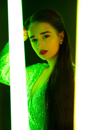 Gorgeous young woman model with bright makeup posing against the backdrop of neon tubes in a dark studio. Close up portrait.の写真素材