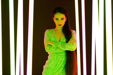 Gorgeous young woman model with bright makeup posing against the backdrop of neon tubes in a dark studio. Close up portrait.の写真素材