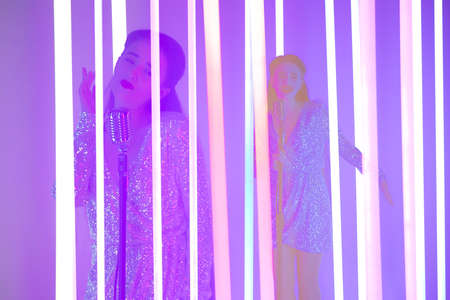Collage of young woman singing into a vintage microphone among bright neon tubes. Close up.の写真素材