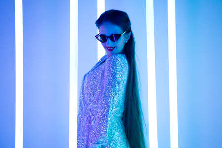 Bright positive trendy studio portrait of a pretty young woman in sunglasses against a background of neon tubes. Sexy style, cute emotions. Close up.の写真素材