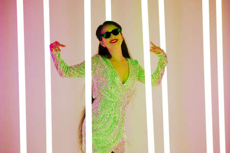 Bright positive trendy studio portrait of a pretty young woman in sunglasses against a background of neon tubes. Sexy style, cute emotions. Close up.の写真素材