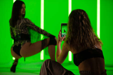 Girls are photographed on a smartphone in the studio against the background of neon lamps with green light.の写真素材