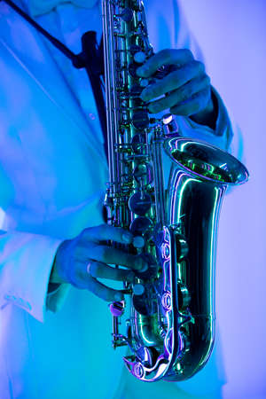 Partial view of stylish professional musician in white suit playing saxophone. Hands and musical instrument close up.の写真素材