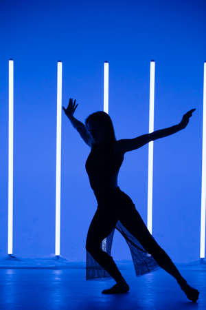 Silhouette of a attractive young woman dancer dancing in a room with neon lamps. Sporty beautiful girl model enjoys a dance in the studio with neon amazing color.の写真素材