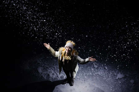 Top view of a happy young woman in a hat and warm clothes among the falling snow on a black background.の写真素材
