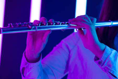 Flute in female hands. Fingers touch flute keys close up. Wind instrument against the background of bright neon lights. Poster for advertising a music school.の写真素材
