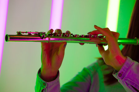 Wind instrument flute close up. Female hands hold a flute against the background of bright neon lights in a dark studio. Poster for advertising a music school.の写真素材