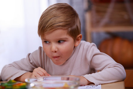 Boy chews sweets with a sly look, sitting at a table with treats for Halloween, in the room on a blurred background. Close up.の写真素材