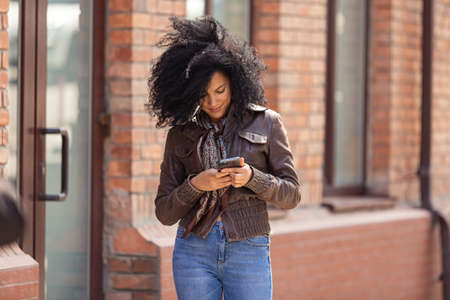 Portrait of young African American woman texting on her smartphone. Brunette with curly hair in...