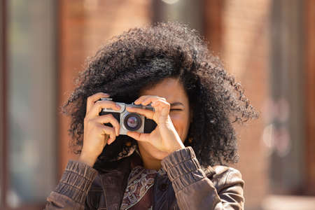 Stylish young African American woman taking pictures with a retro camera. Brunette with curly hair...
