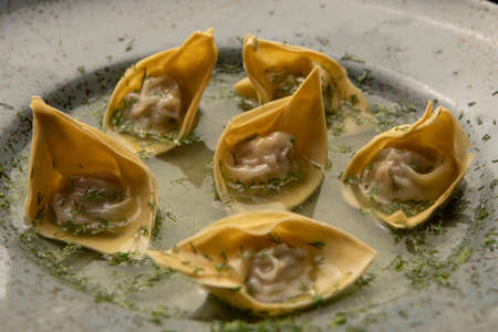 Fresh wonton dumplings with meat are presented on a round gray plate close up. Restaurant serving food, Chinese traditional dumplings sprinkled with dill. Chinese cuisine. Asian steam food dim sum.の写真素材