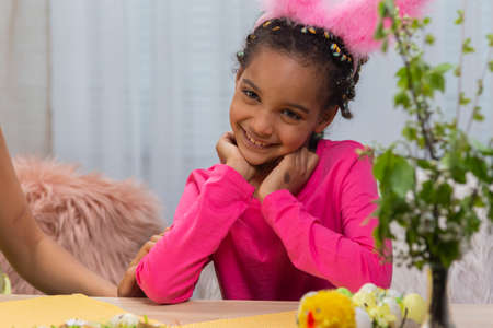 A cute little girl in funny pink bunny ears smiles. African American child posing against the backdrop of a light room. Happy easter. Close up.の写真素材
