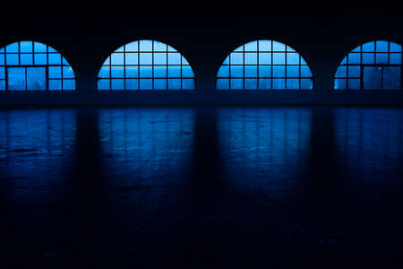 Beautiful empty dark skating rink illuminated with soft blue light. An ice arena with smooth, shiny ice surface and reflective shadows. Concept of winter sports, figure skating and hockey.の写真素材