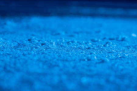 Ice background and texture with scratches from skating and hockey. Ice rink floor, detail of textured ice background with snow and crystals in blue light. Empty ice rink close up.の写真素材